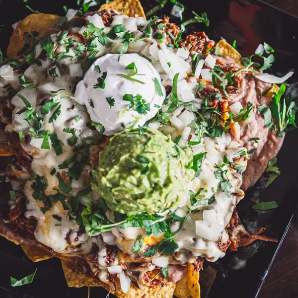 Loaded nachos with melted cheese, shredded meat, refried beans, guacamole, sour cream, and cilantro.