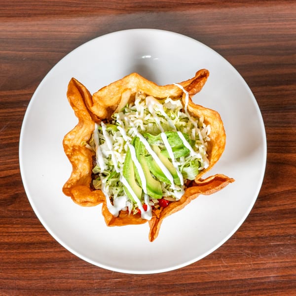 Taco salad in a crispy fried tortilla bowl, topped with lettuce, avocado, and sour cream.