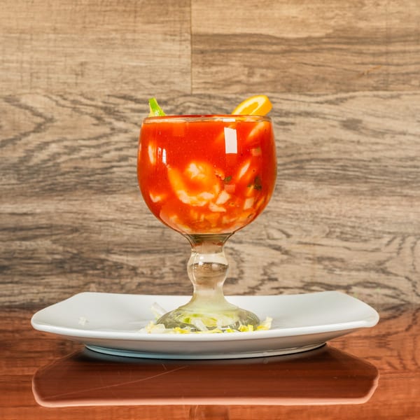 A Mexican shrimp cocktail in a goblet, garnished with lime and orange, on a white plate.