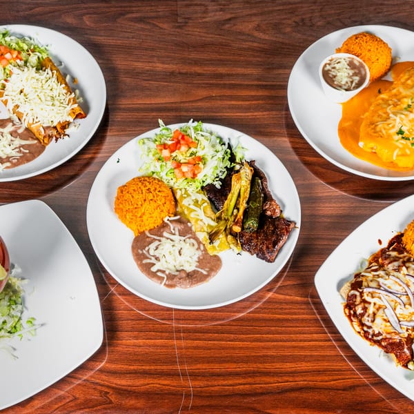 Four plates of various Mexican dishes, including tacos, enchiladas, and carne asada, on a wooden table.