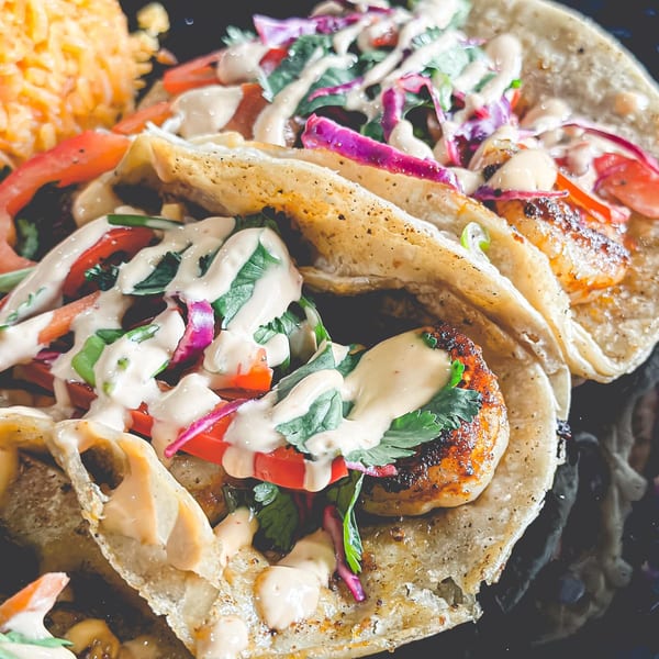 Two grilled shrimp tacos with red cabbage, tomatoes, cilantro, and creamy sauce, served with rice.