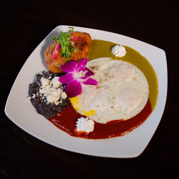 A Mexican breakfast plate with fried eggs, black beans, a fried pastry, and two sauces.
