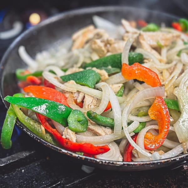 Sizzling fajitas with chicken, green and red bell peppers, and onions in a cast iron pan.