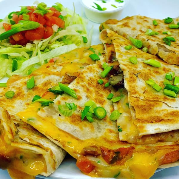 Cheesy quesadillas topped with green onions, served with shredded lettuce, diced tomatoes, and sour cream.