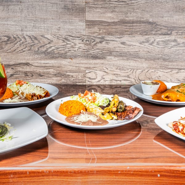 Multiple plates of Mexican food, including tacos, enchiladas, rice, and beans, on a wooden table.