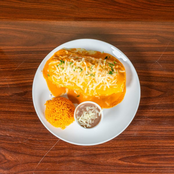 A large burrito covered in orange sauce, shredded cheese, and cilantro, served with rice and beans.