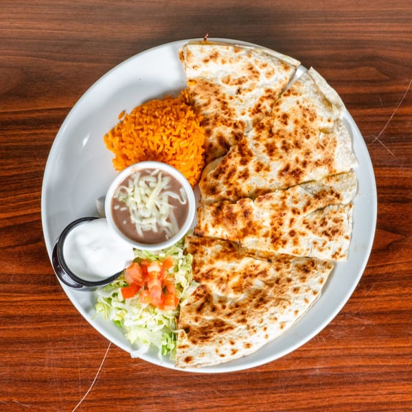 A quesadilla with rice, refried beans, sour cream, and a side salad on a white plate.