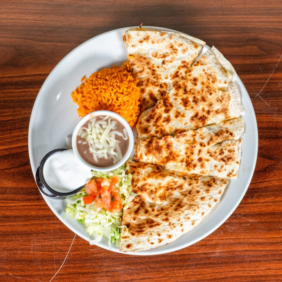 A quesadilla with rice, refried beans, sour cream, and a side salad on a white plate.