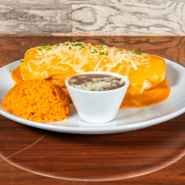 A large, cheese-covered burrito with orange sauce, rice, and a side of beans on a white plate.
