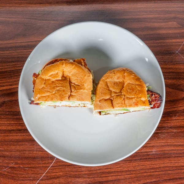 A Mexican torta sandwich, cut in half, revealing layers of meat, lettuce, and sauce on a white plate.