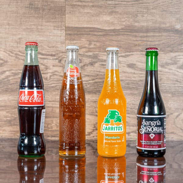 Four Mexican sodas: Coca-Cola, Sidral Mundet, Jarritos Mandarin, and Sangría Señorial on a reflective surface.